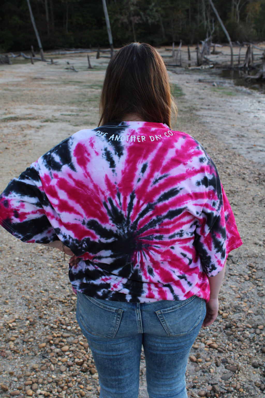 Person wearing a pink and black tie-dye tshirt with jeans on a textured surface