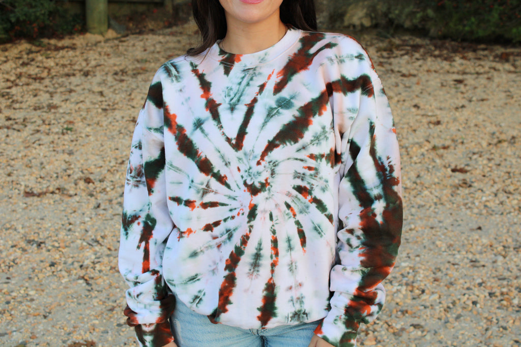 Person wearing a tie-dye sweatshirt with a spiral pattern outdoors.