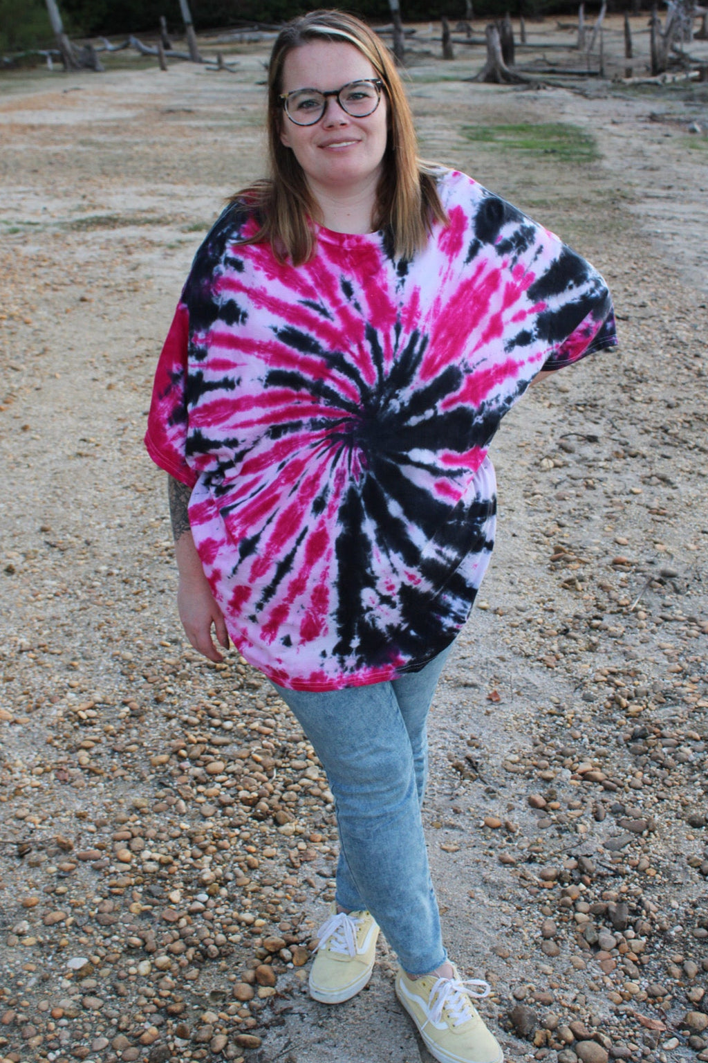 Person wearing a tie-dye shirt standing on a gravel path