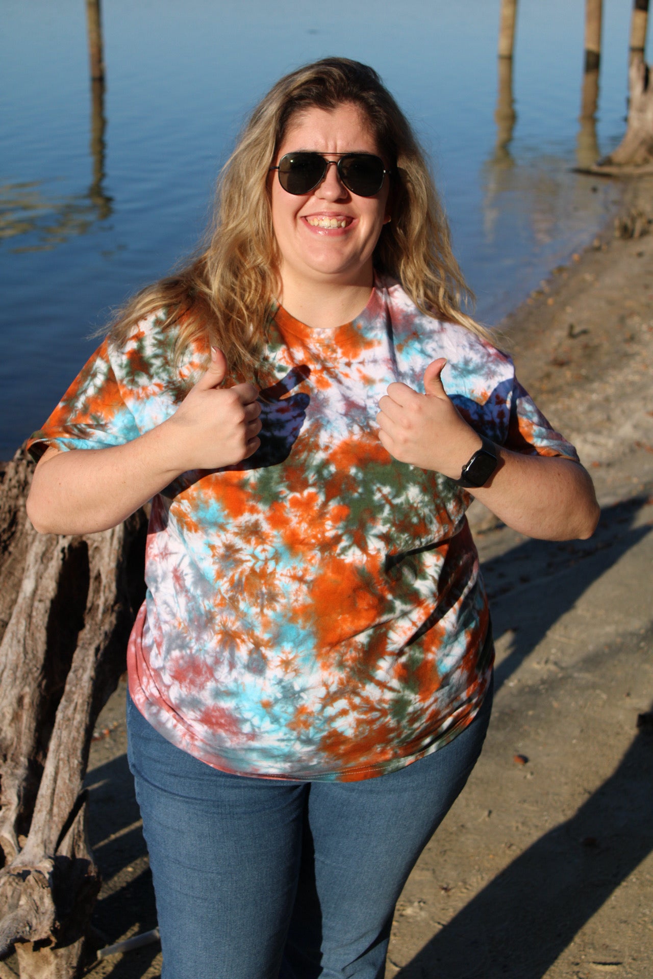 Person wearing a colorful shirt and sunglasses by a blue wall with wooden planks.